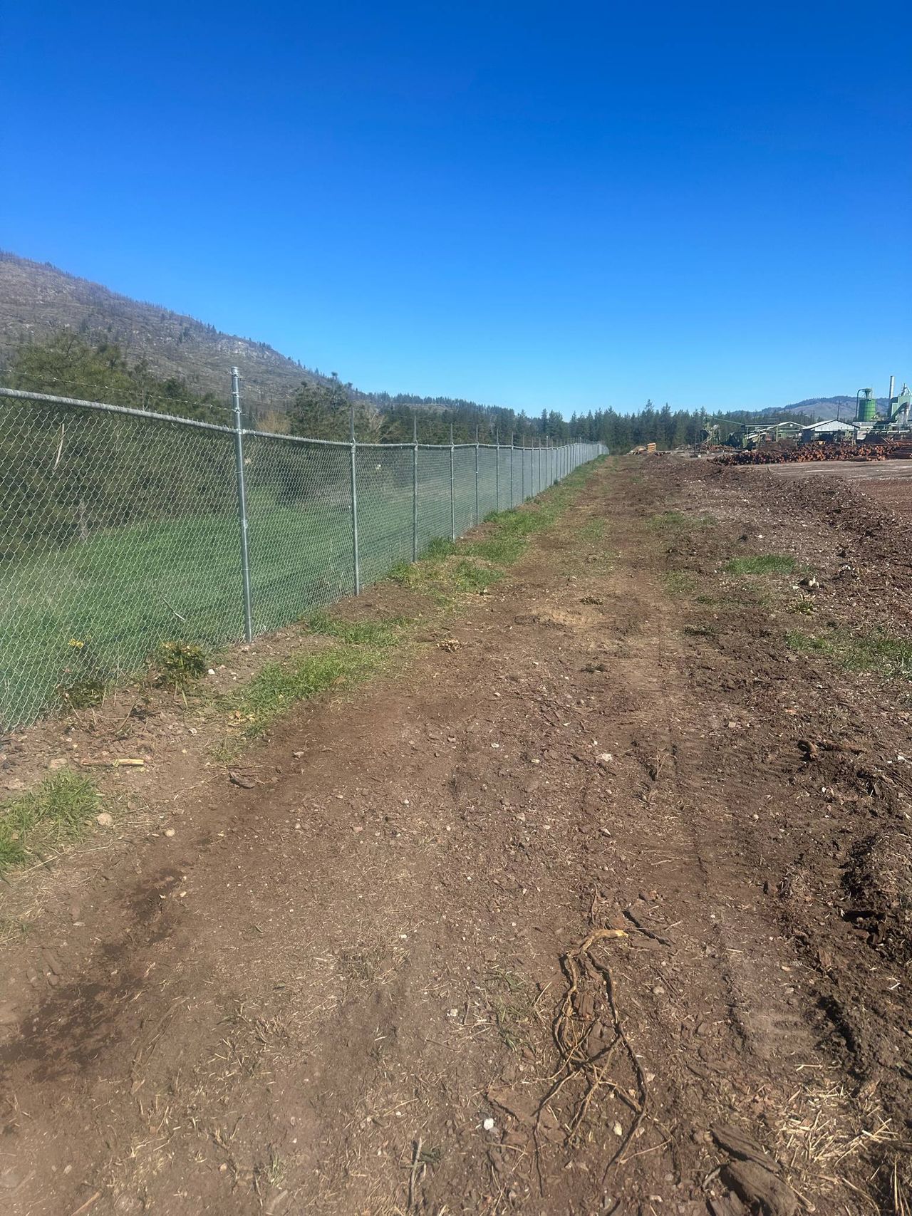 Galvanized chain-link security fence with barbed-wire top arms running along a commercial mill yard