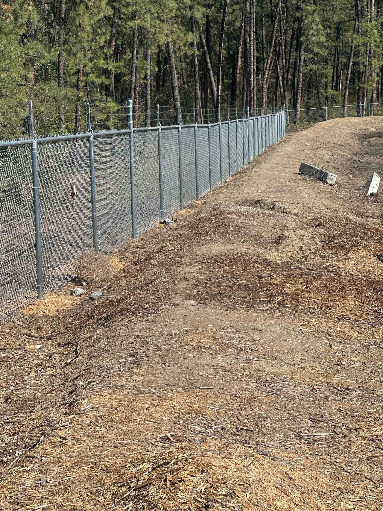 Industrial security fencing installation featuring a six-foot-tall chain-link perimeter topped with two strands of sharp razor wire around a commercial property.