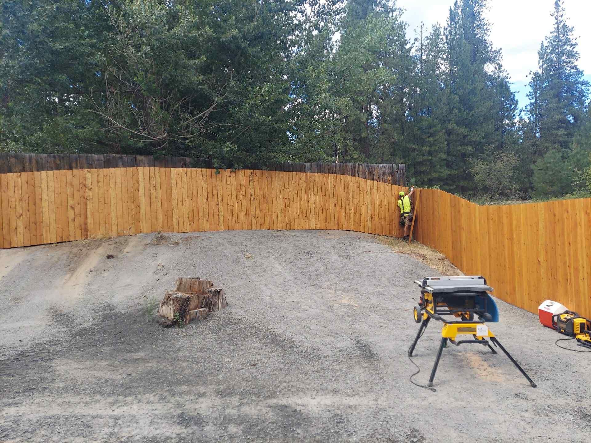 A Vance Fabrication crew member fitting a panel on a long stained cedar privacy fence.
