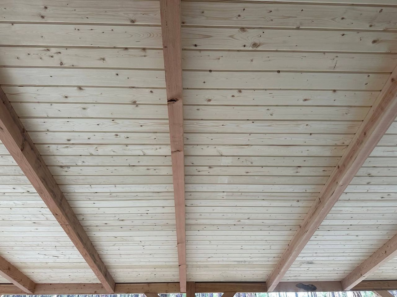 Interior view of handcrafted structural heavy timber framing showcasing interlocking joinery and a tongue and groove wood plank ceiling.