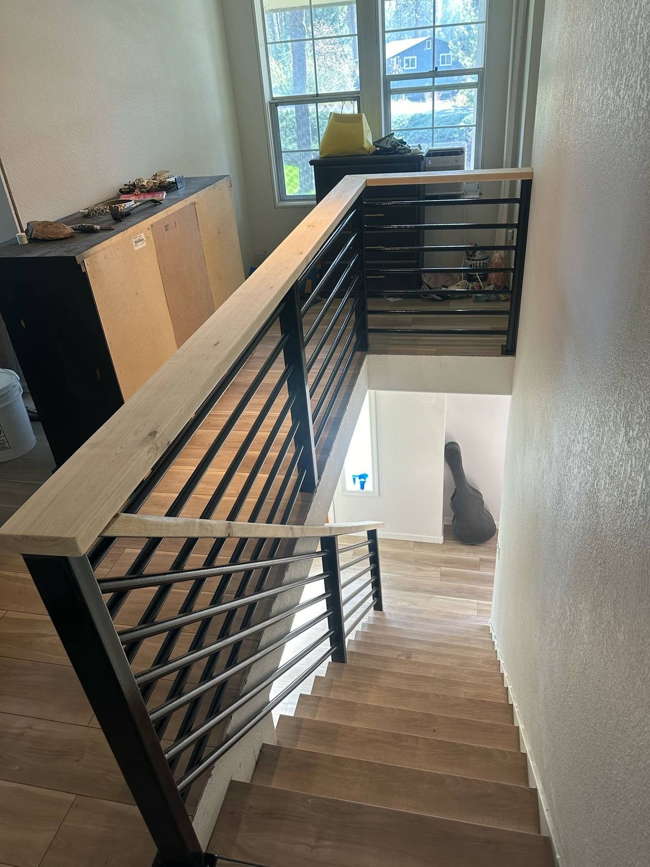 Custom welded steel stair railing with horizontal bar infill and a solid wood handrail inside a home