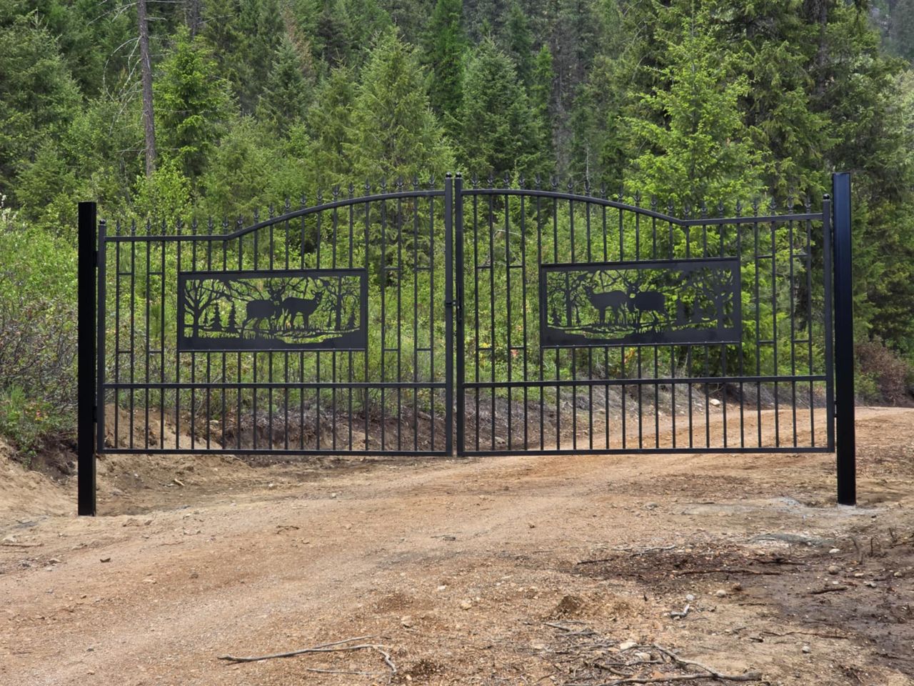 Custom ornamental iron driveway gate with a laser-cut elk and forest scene, hung on welded steel posts