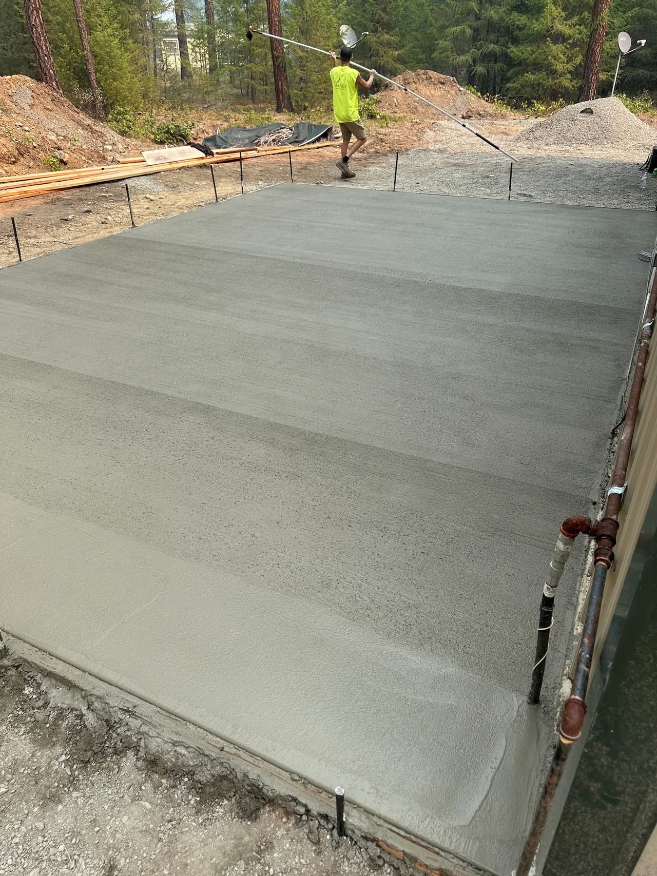 A freshly poured reinforced concrete pad foundation with integrated structural footings engineered for a heavy timber-framed lean-to structure.