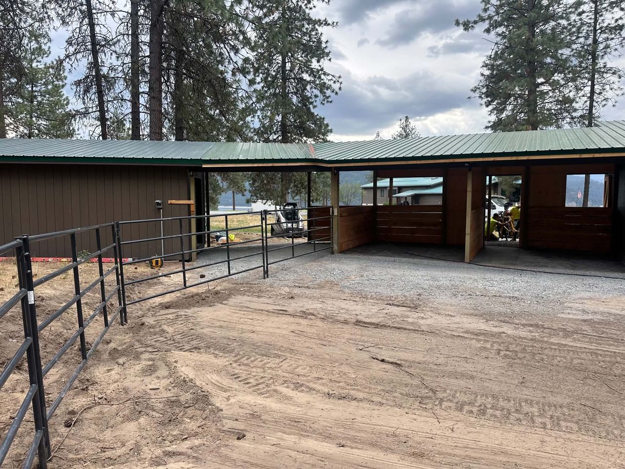 Welded steel pipe corral panels and swing gate at a horse barn with covered stalls and cedar kick walls.