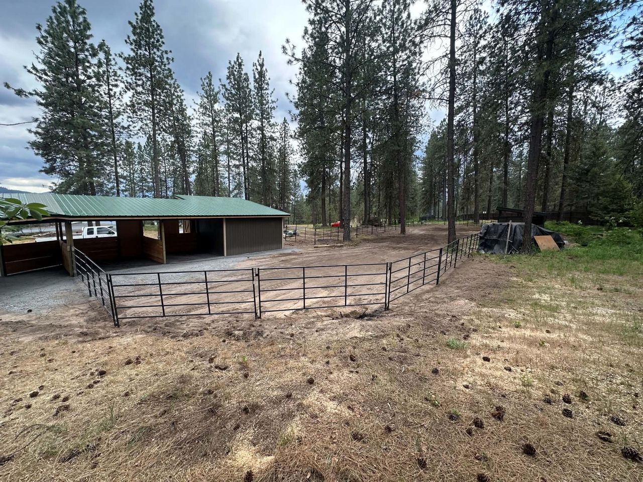 Welded steel pipe corral panels and gates enclosing a livestock paddock beside a barn in a stand of ponderosa pines
