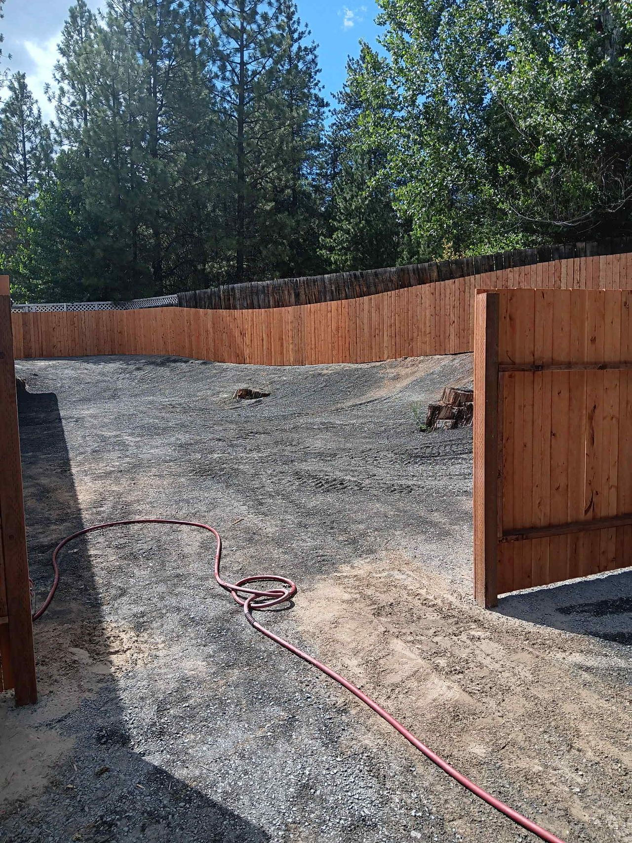 Stained cedar privacy fence with a wide double-gate opening onto a gravel driveway